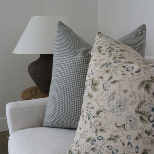 Floral-patterned pillow on a light gray sofa with a lamp in the background.