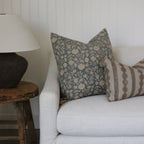 White sofa with patterned pillows against a white wall, wooden side table with lamp.